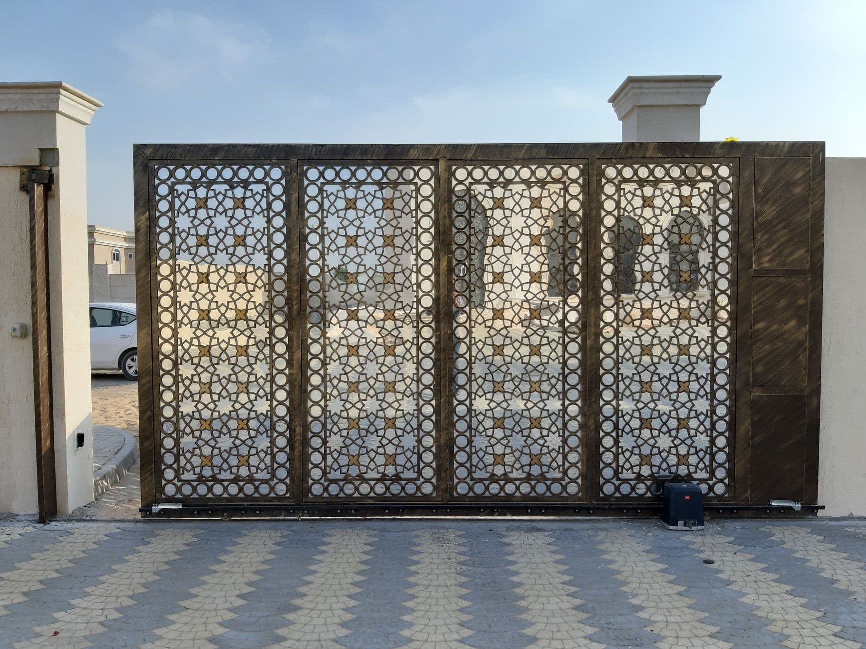 A sliding metal gate with a cut-out geometric pattern, its drive motor and toothed rail visible along the base.