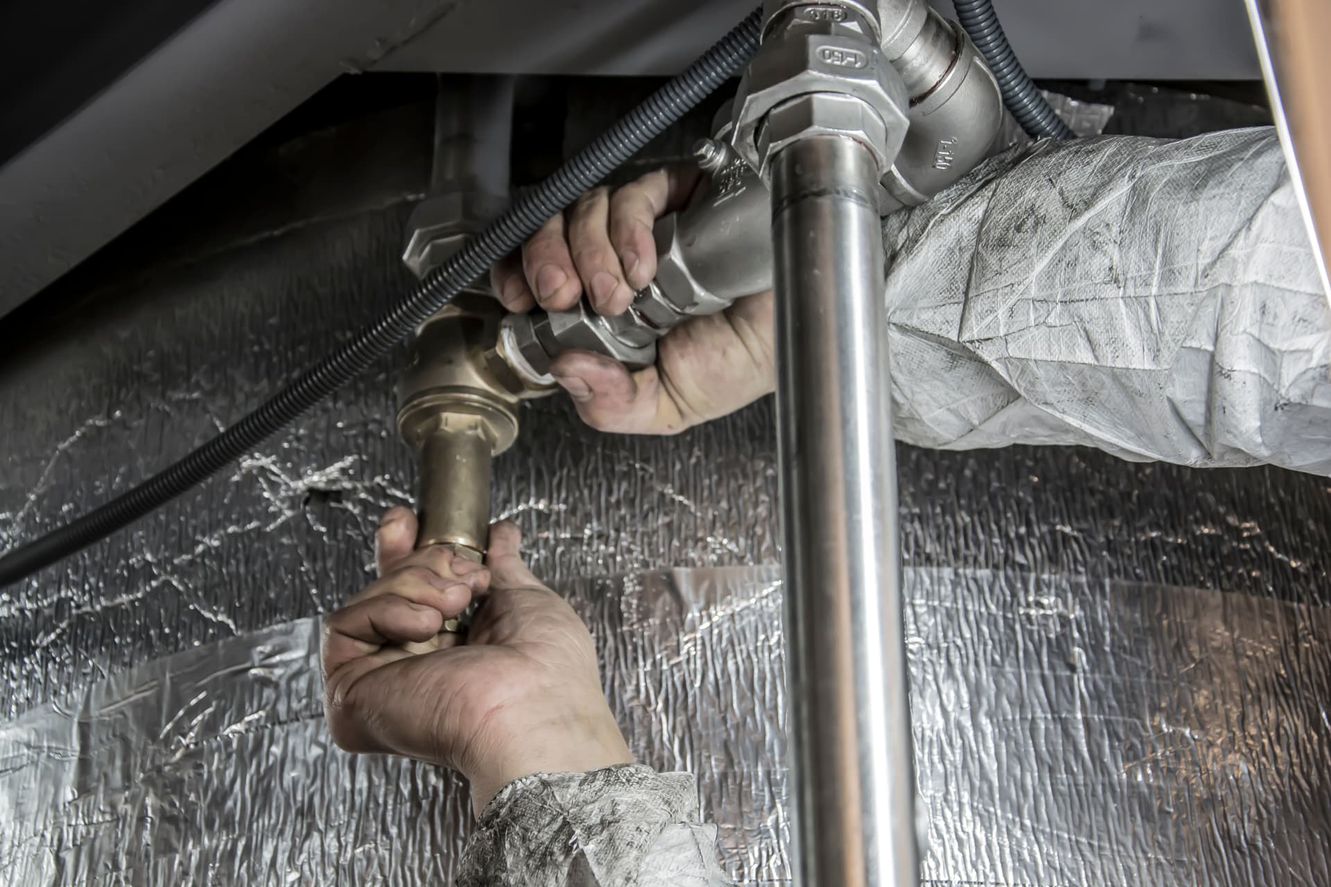 Two hands fitting a brass valve onto insulated pipework.