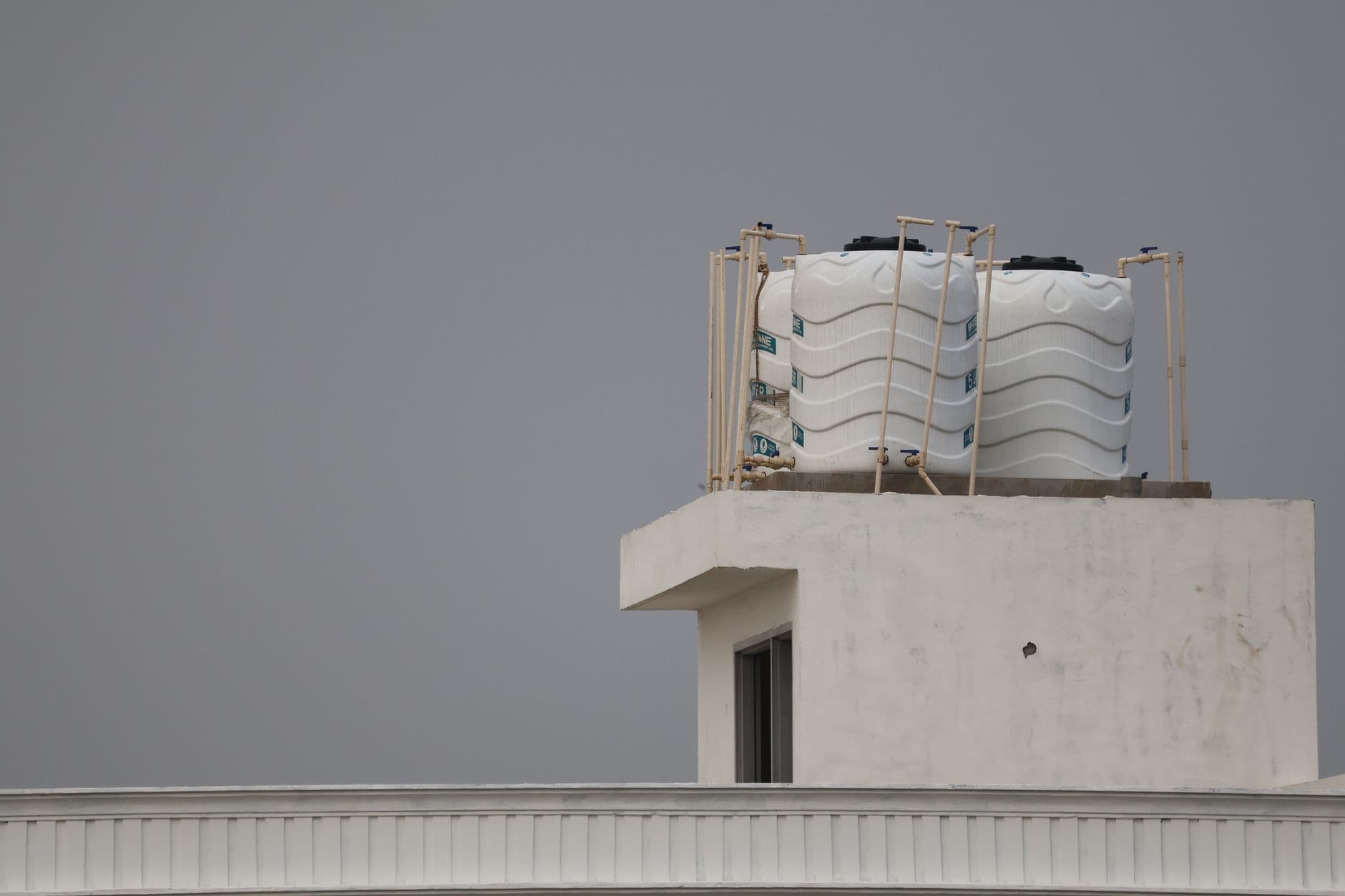 Two white polyethylene water storage tanks on a flat roof, connected by pipework with isolation valves.