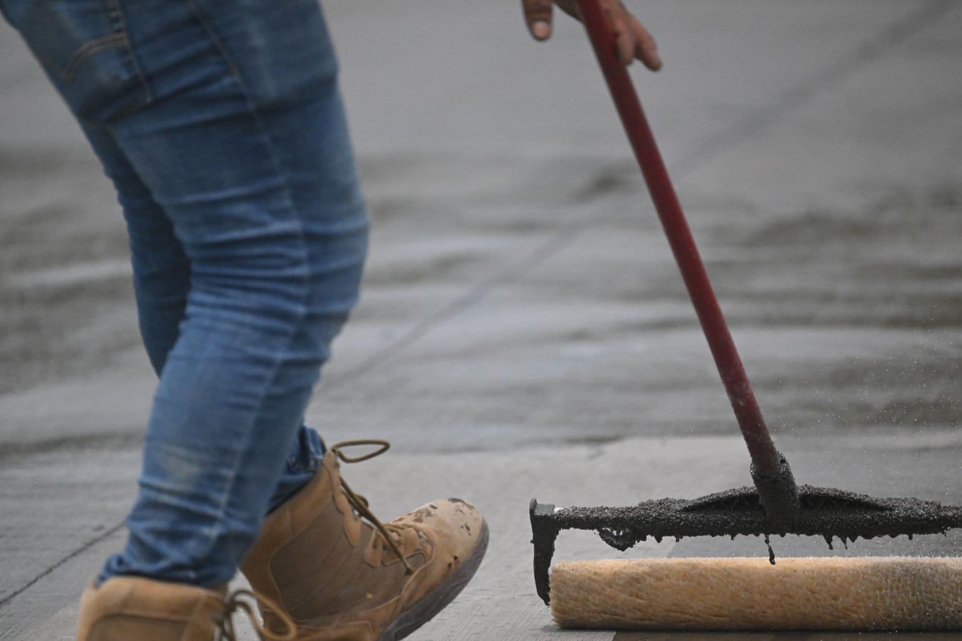 A squeegee spreading black waterproofing compound across a concrete surface.